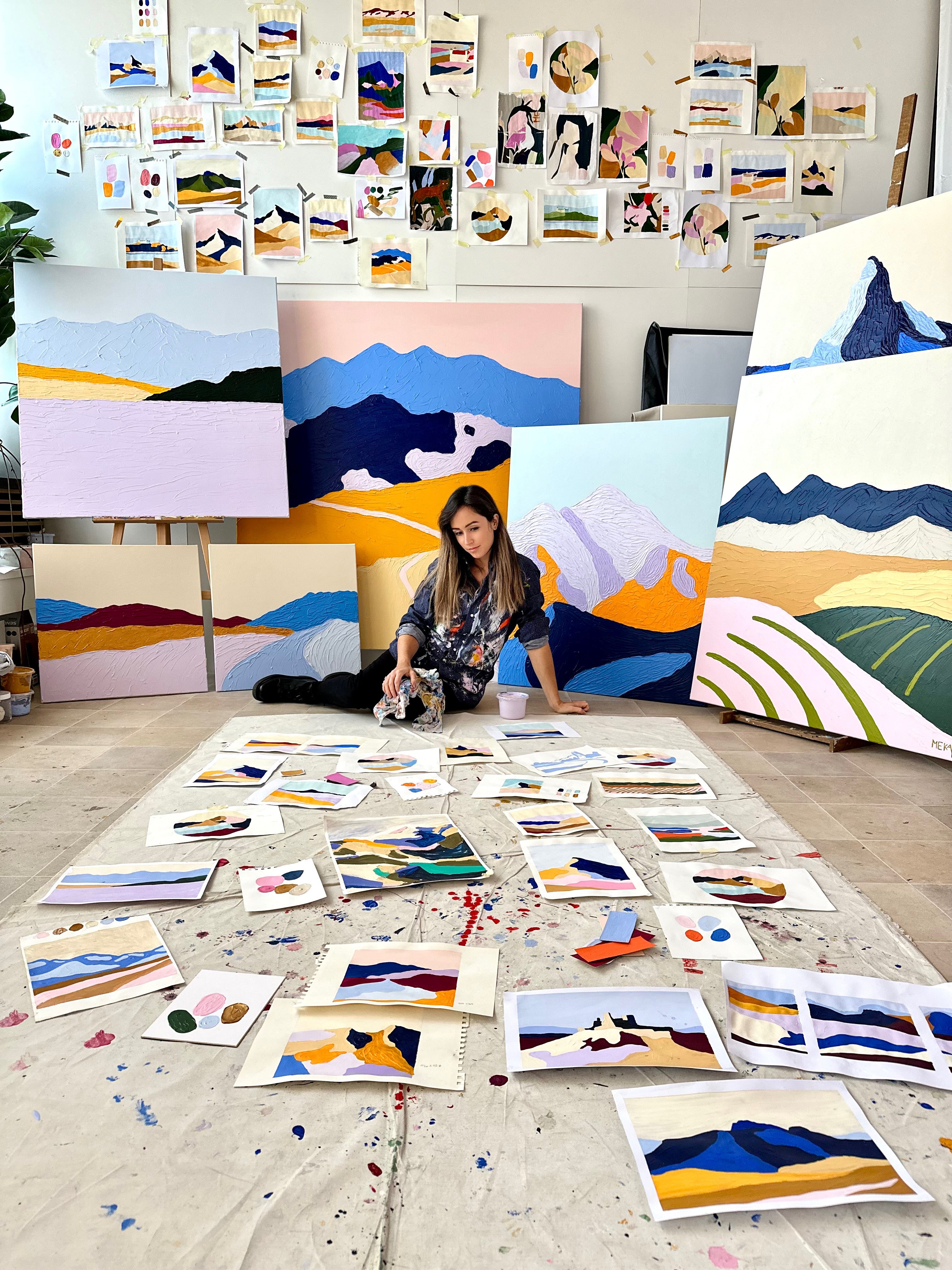 Artist Meka Klimeková working in her studio surrounded by textured abstract mountain paintings and sketches, contemporary art creation process