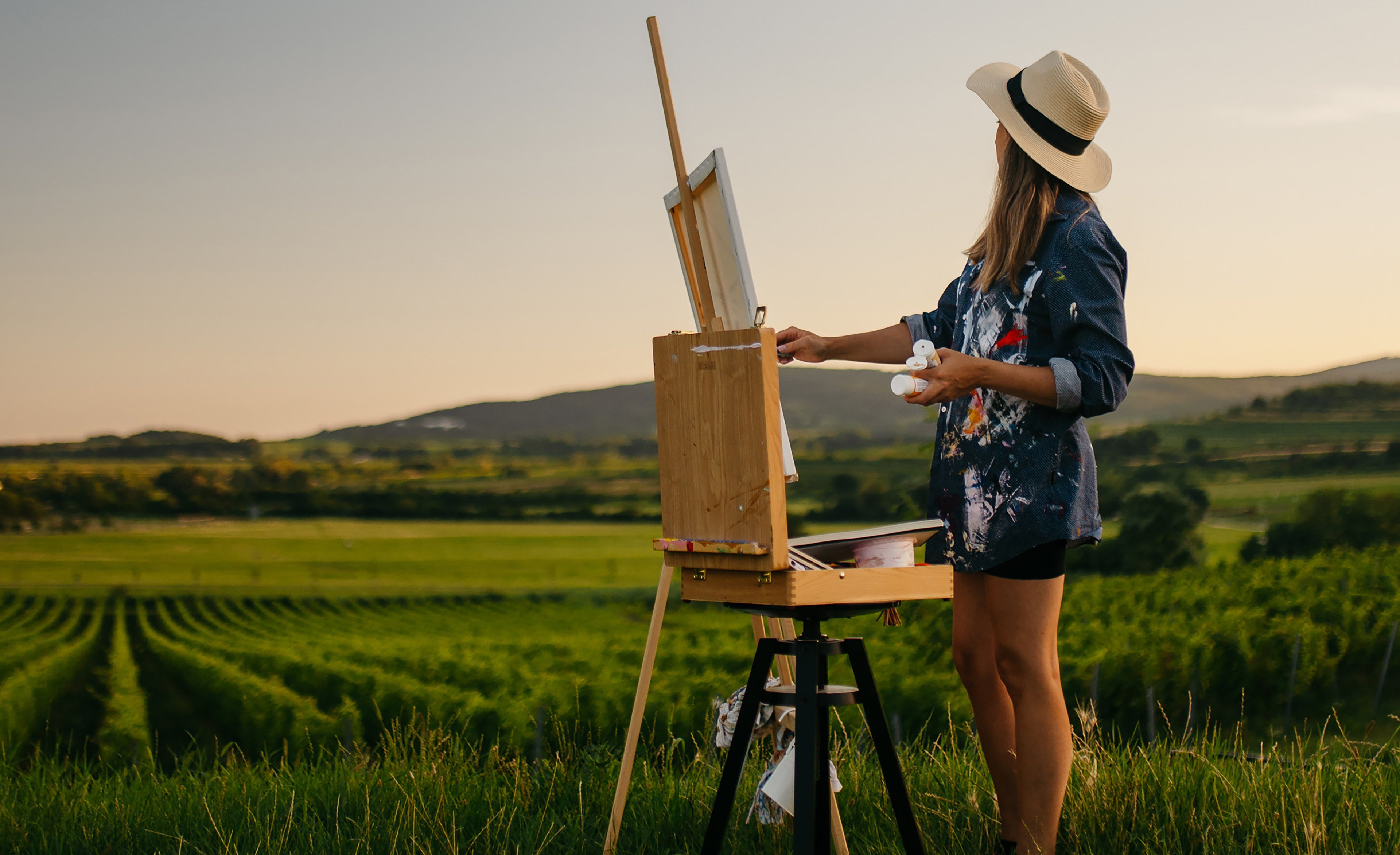 Artist Meka Klimeková painting outdoors at an easel during golden hour, contemporary abstract art process in nature